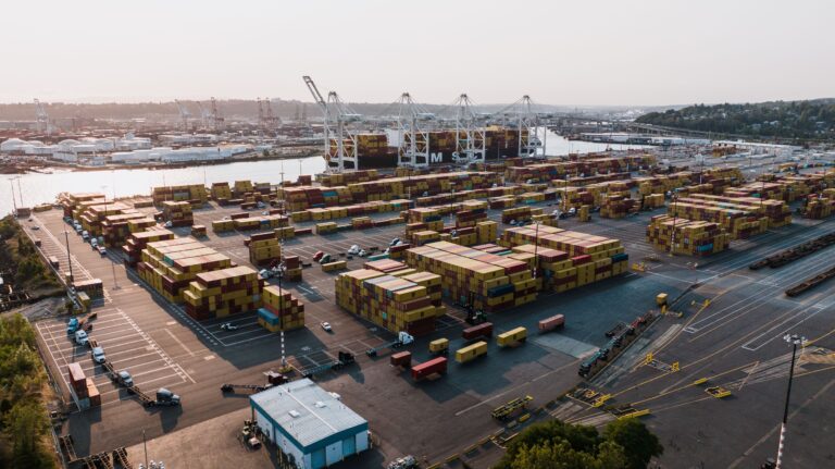 Aerial view of stacked shipping containers and gantry cranes at a busy Southern California port.